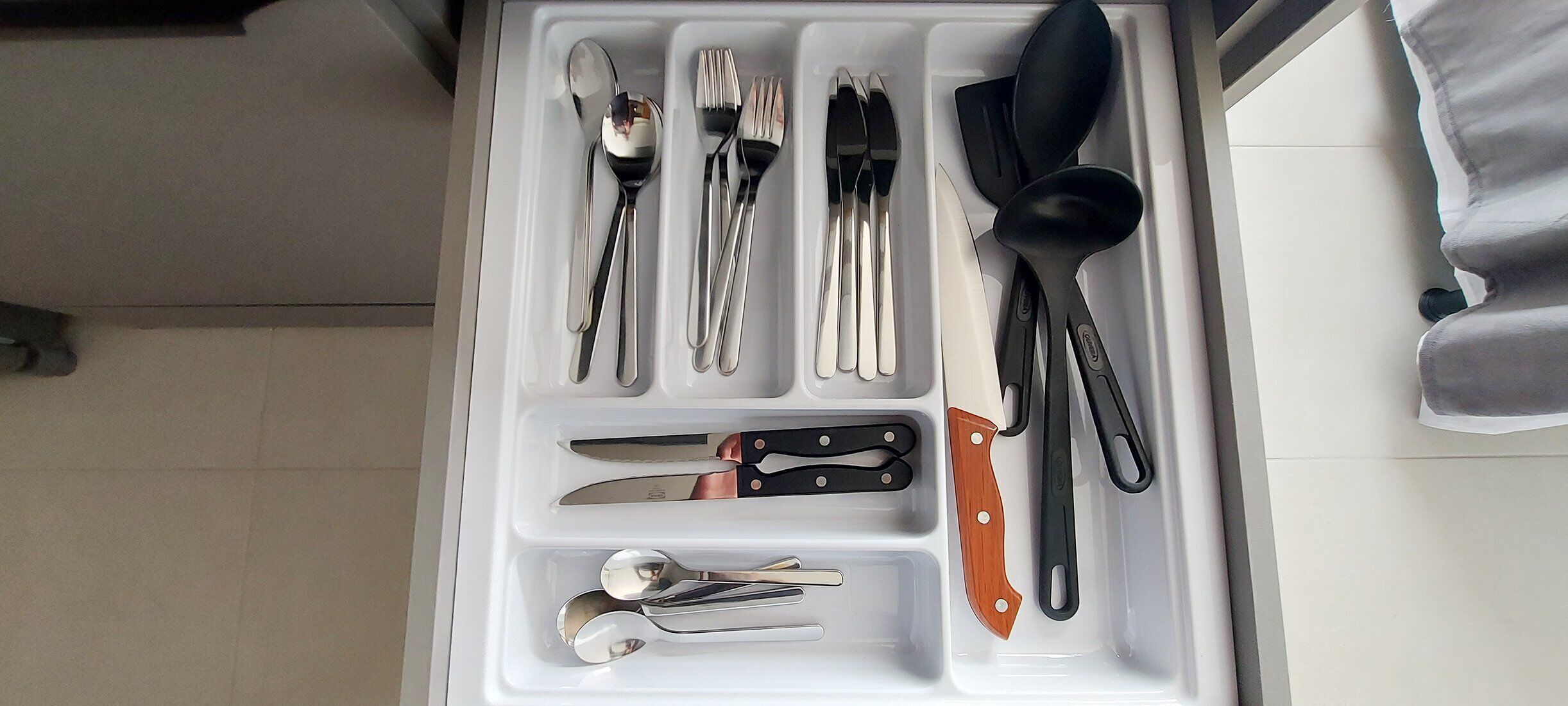 Eine Schublade mit verschiedenen Küchenutensilien, darunter Löffel, Gabeln, Messer und ein Pfannenwender.