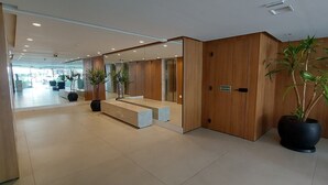 A modern hotel lobby with a reception desk, wooden paneling, and potted plants. - COBAR0121 - Edifício Barra Premium (Salvador)