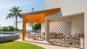 Um pátio externo com móveis de madeira, uma piscina e vista para o oceano.