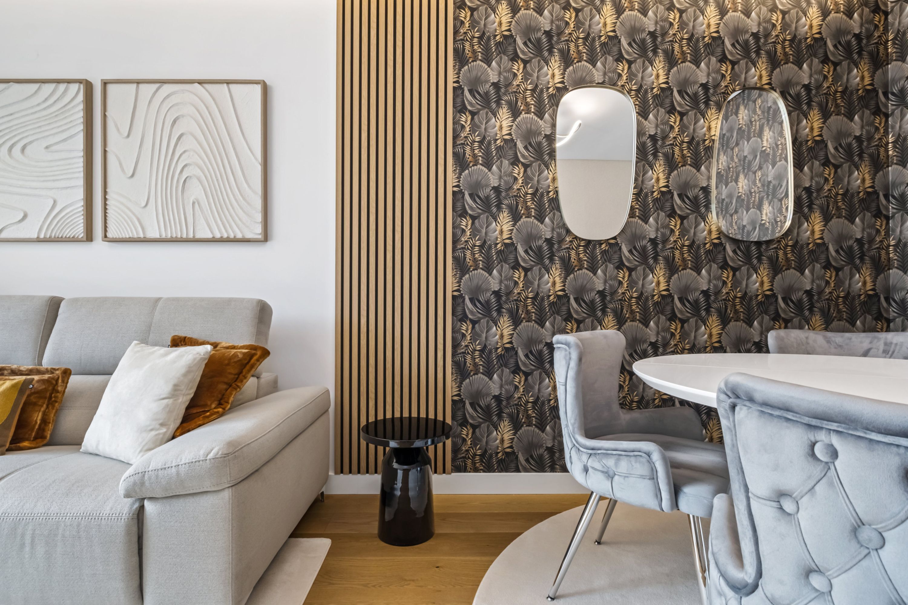 Ein modernes Wohnzimmer mit einem grauen Sofa, einem runden Esstisch und einer Wand mit Muster.