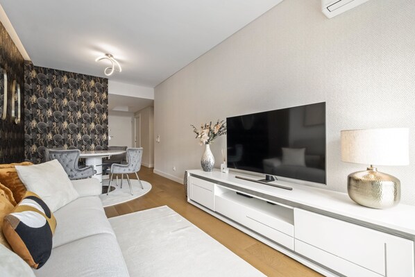 A modern living room with a flat-screen TV, white entertainment unit, and a dining area with a table and chairs. - Ocean s Glow by Homie (Funchal)