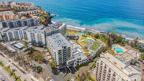 Vista aérea de um complexo hoteleiro à beira-mar, com vários edifícios, piscina e vista para o oceano.