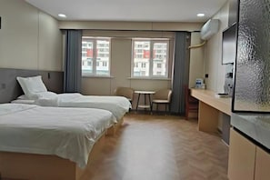 A hotel room with two beds, a small table, a chair, and a window with a view of buildings.