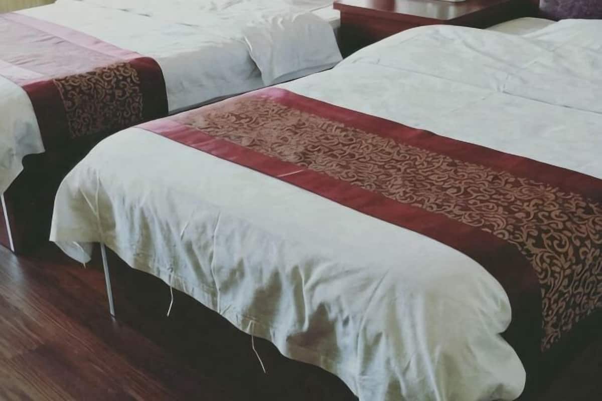 Una habitación de hotel con dos camas, piso de madera y colcha estampada en rojo y blanco.