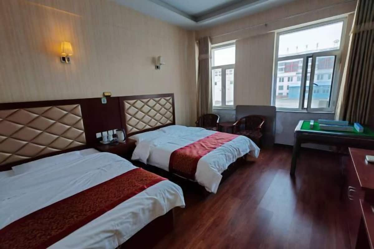 Habitación de hotel con dos camas, un escritorio, una silla y una ventana con vistas a edificios.
