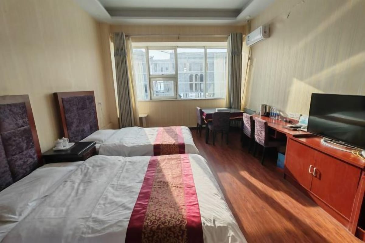 A hotel room with two beds, a desk, a television, and a window with curtains.
