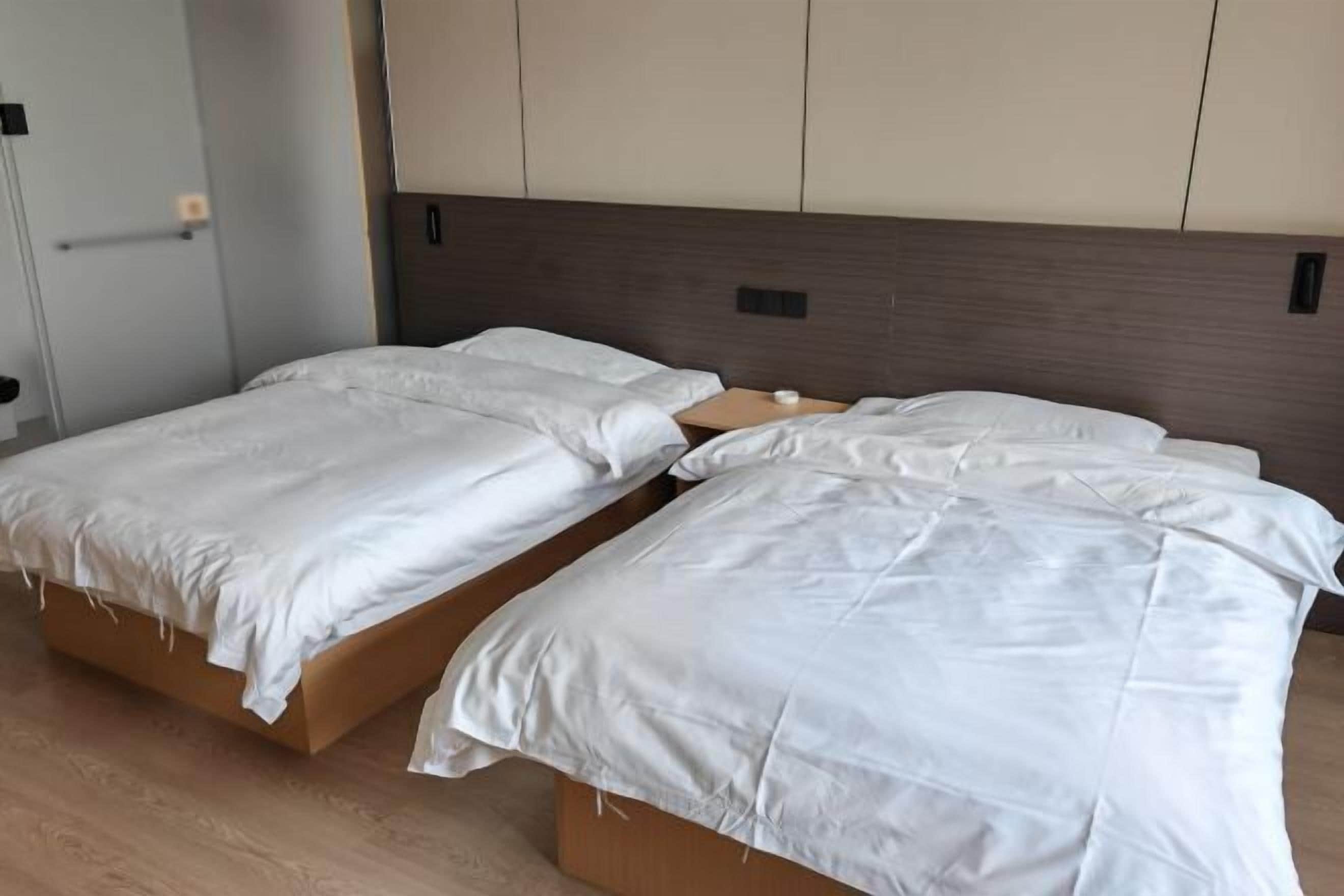 A room with two single beds, wooden headboards, and a light-colored wall.