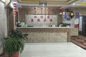 Una recepción con mostrador de mármol, adornos colgantes rojos y un reloj en la pared.