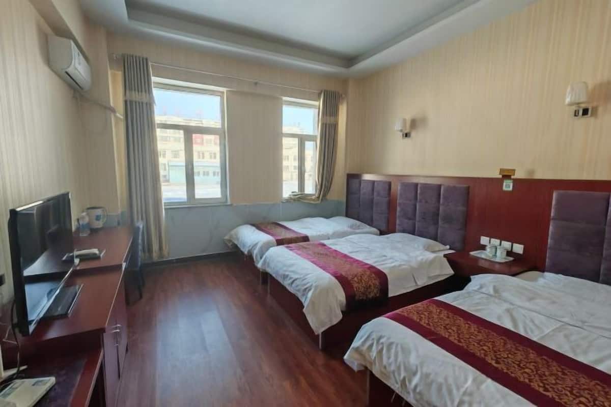 Una habitación de hotel con dos camas, un escritorio con computadora, un televisor y una ventana con cortinas.