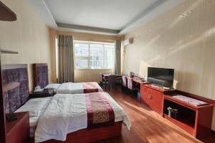 A hotel room with two beds, a desk, a television, and a window with curtains.