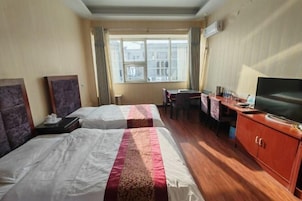 Habitación de hotel con dos camas, un escritorio con silla, televisor y ventana con cortinas.