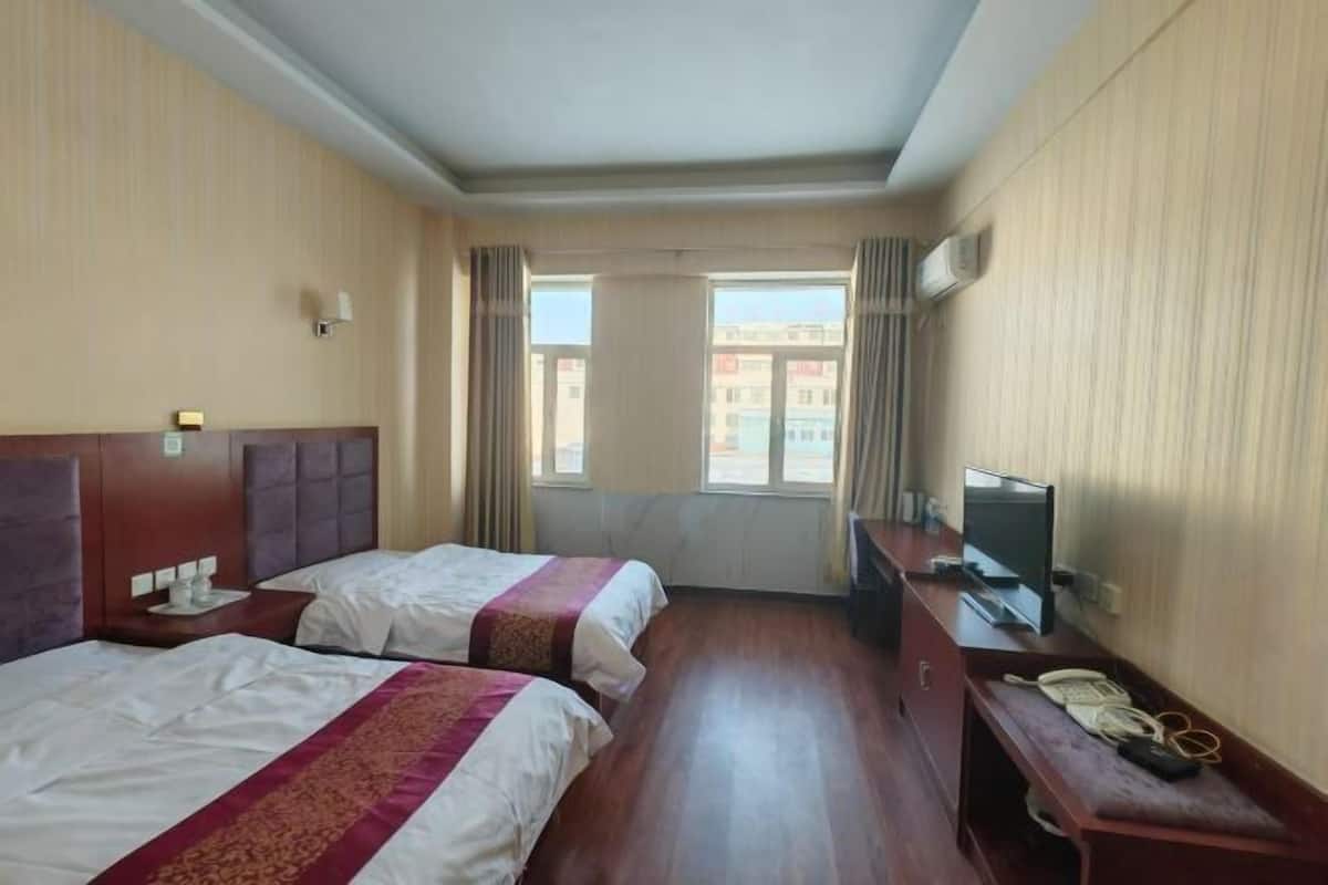 Habitación de hotel con dos camas, un escritorio con televisor, teléfono y ventana con cortinas.