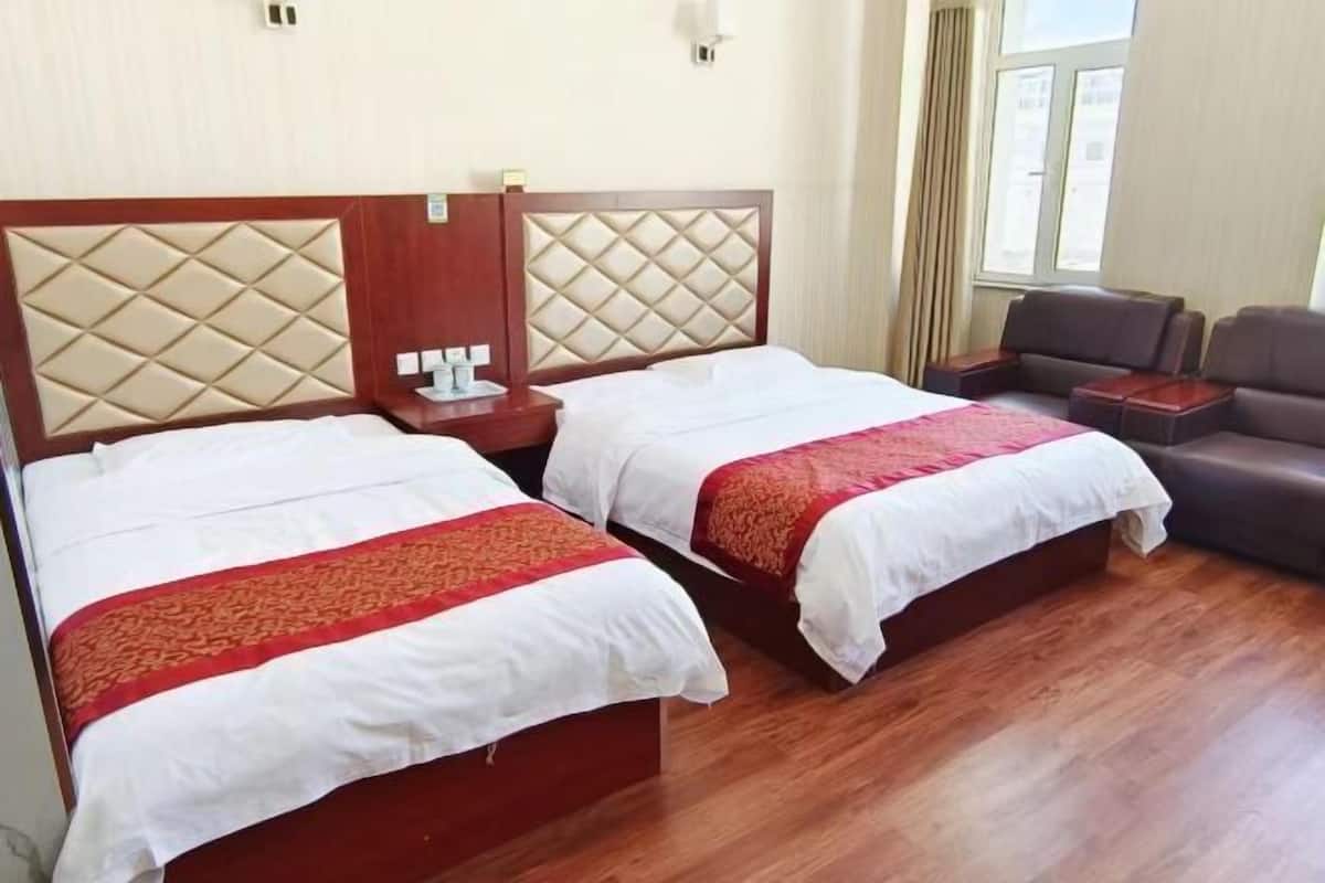 Una habitación de hotel con dos camas, un sofá, una mesita de noche y una ventana.