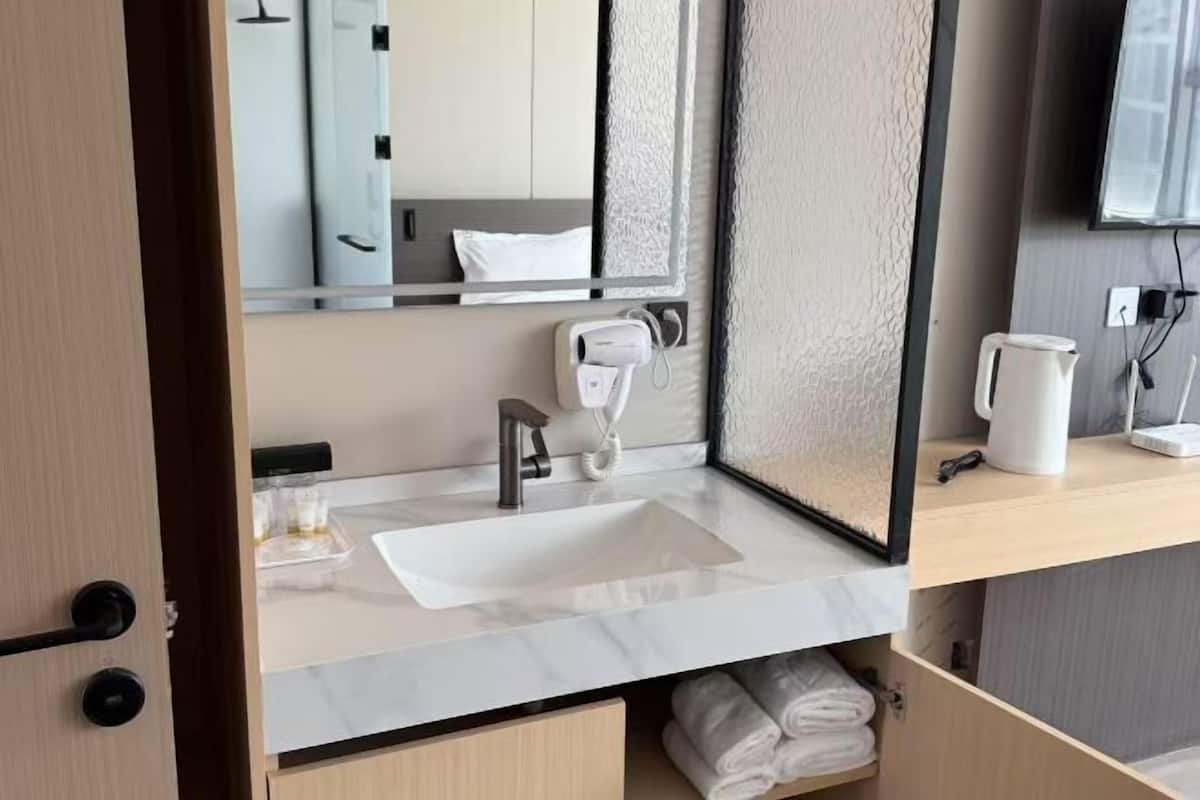 Un baño moderno con un espejo grande, un lavabo, un secador de pelo y un perchero para toallas.