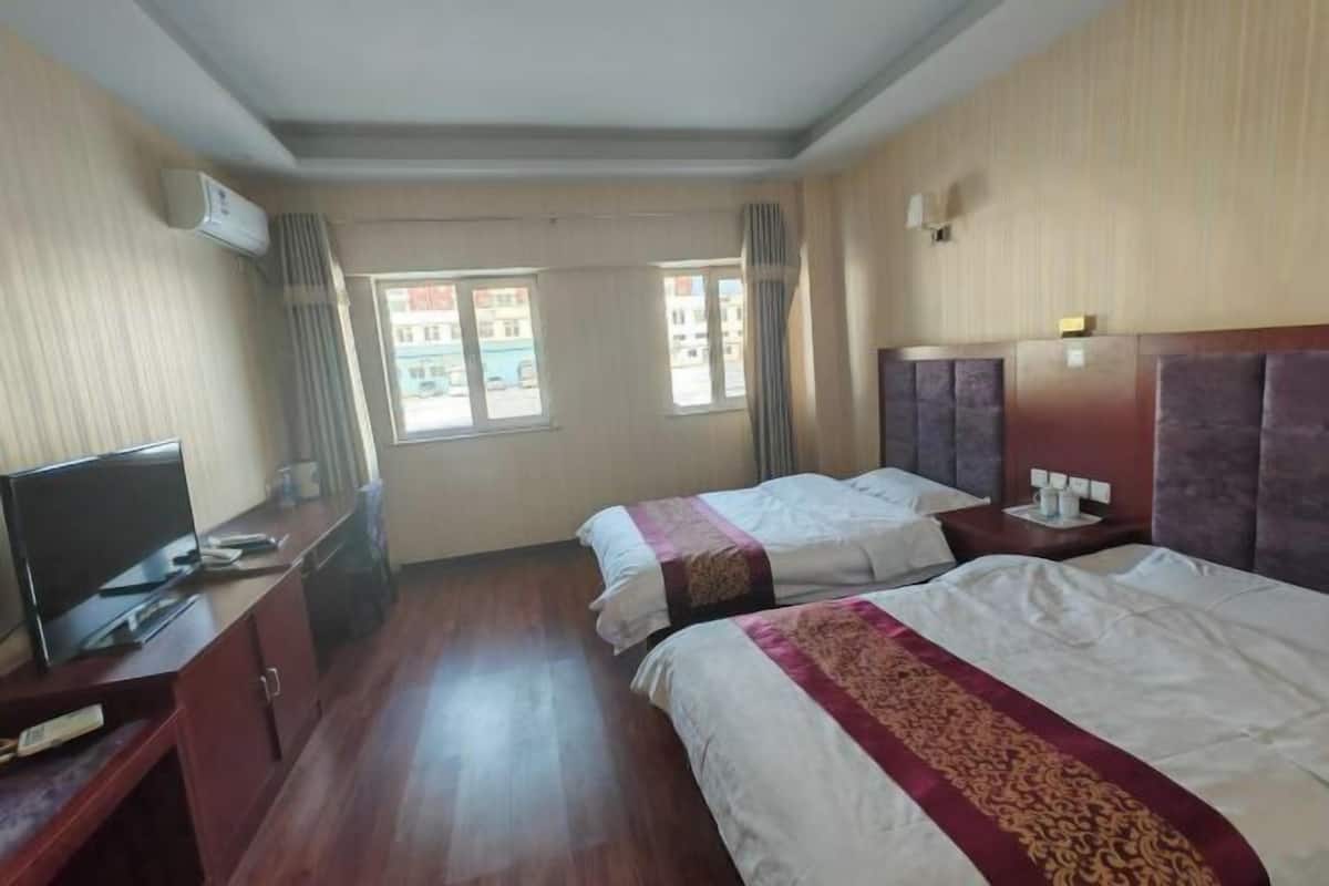 Habitación de hotel con dos camas, televisión y ventana con cortinas.