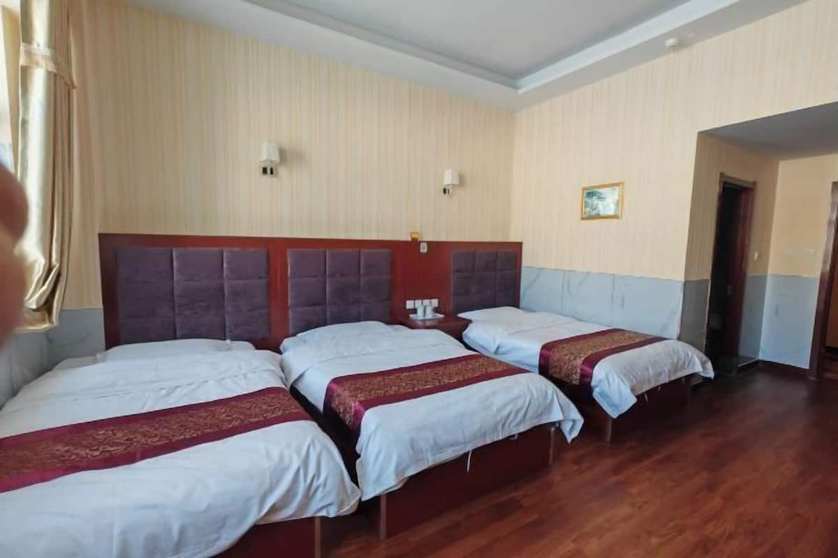 Una habitación de hotel con tres camas, cada una con cabecera y mesita de noche.