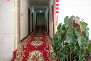 Un pasillo con alfombra roja, una planta y adornos rojos colgantes.