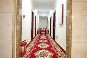 Un pasillo con alfombra roja, extintores e detector de incendios en la pared.