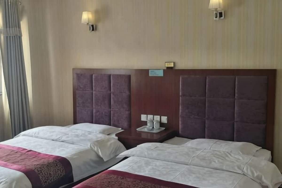 Habitación de hotel con dos camas, una mesita de noche con lámpara y una lámpara de pared.