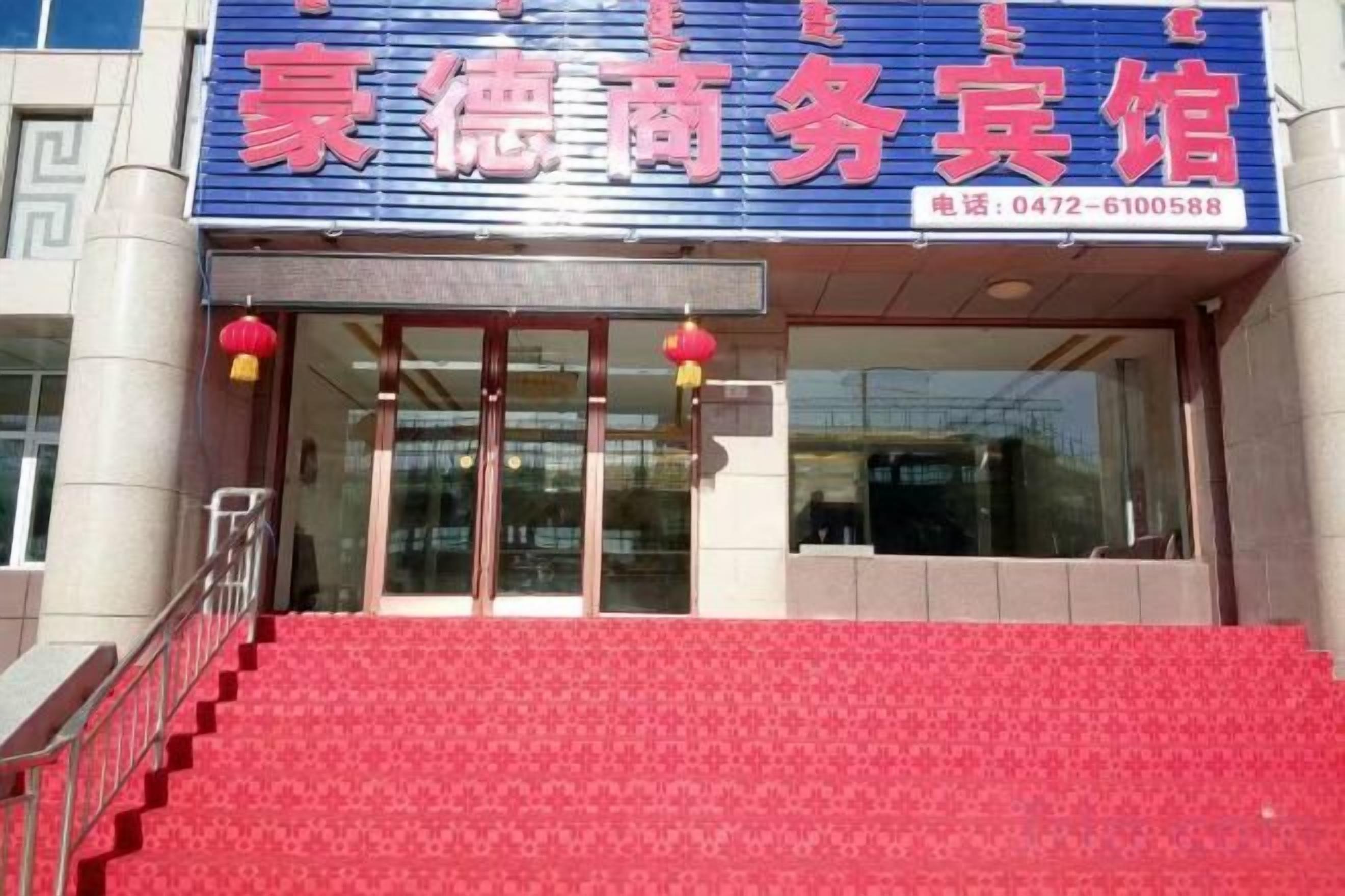 A hotel entrance with a red carpet, glass doors, and a blue sign with red lettering.