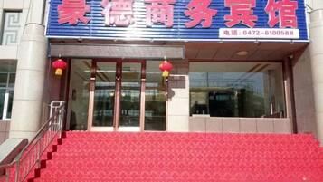 A hotel entrance with a red carpet, glass doors, and a blue sign with red lettering.