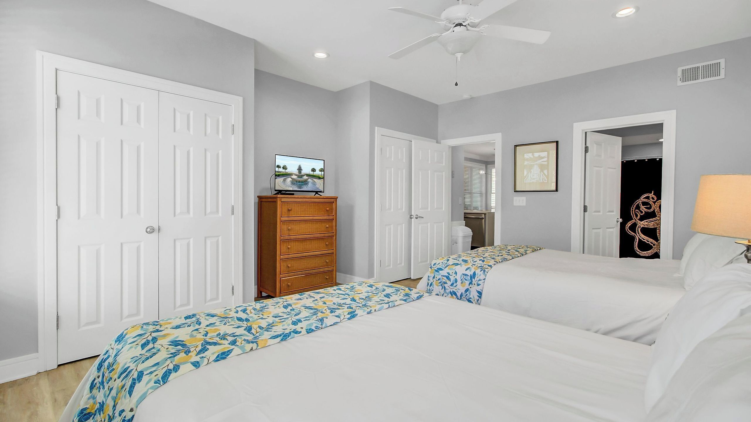 A bedroom with two beds, a dresser, a ceiling fan, and a television.