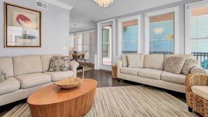 A modern living room with two sofas, a coffee table, and a chandelier. - 125 Grand Pavillion by Avantstay Steps From Sand (Isle of Palms)