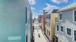 A narrow street with buildings on both sides, a clear sky, and a distant view of a body of water. - 125 Grand Pavillion by Avantstay Steps From Sand (Isle of Palms)