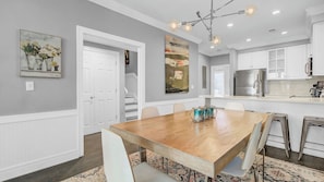 A modern kitchen with a stainless steel refrigerator, a dining area with a wooden table and chairs, and a staircase leading to another level.