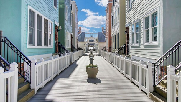 A wooden boardwalk leading to a central archway between colorful buildings. - 125 Grand Pavillion by Avantstay Steps From Sand (Isle of Palms)