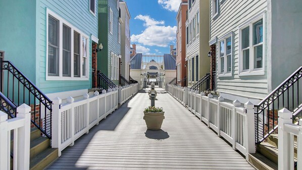 A wooden boardwalk leading to a central archway between colorful buildings.