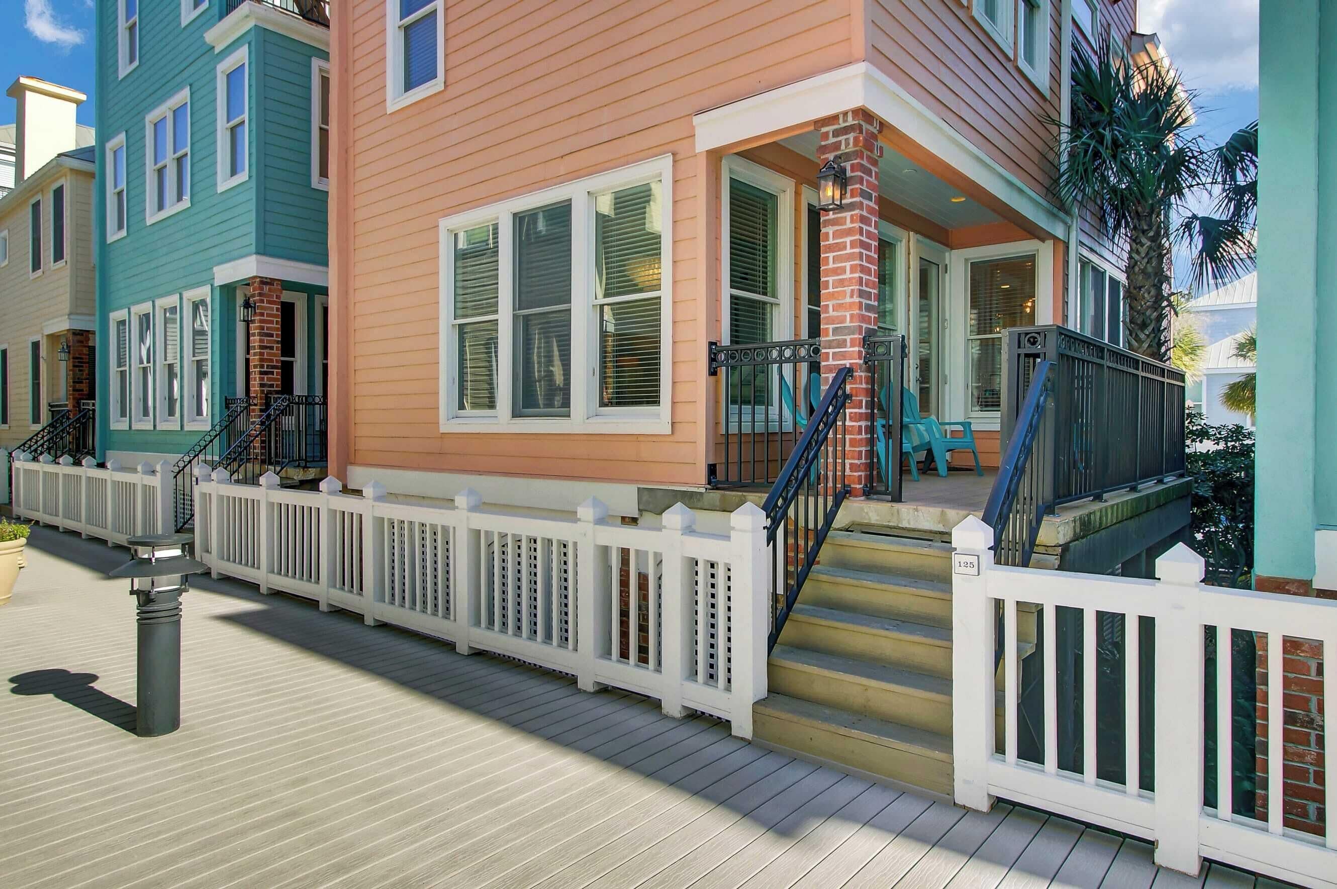 A row of colorful townhouses with white picket fences, a wooden deck, and a brick staircase leading to the entrance.
