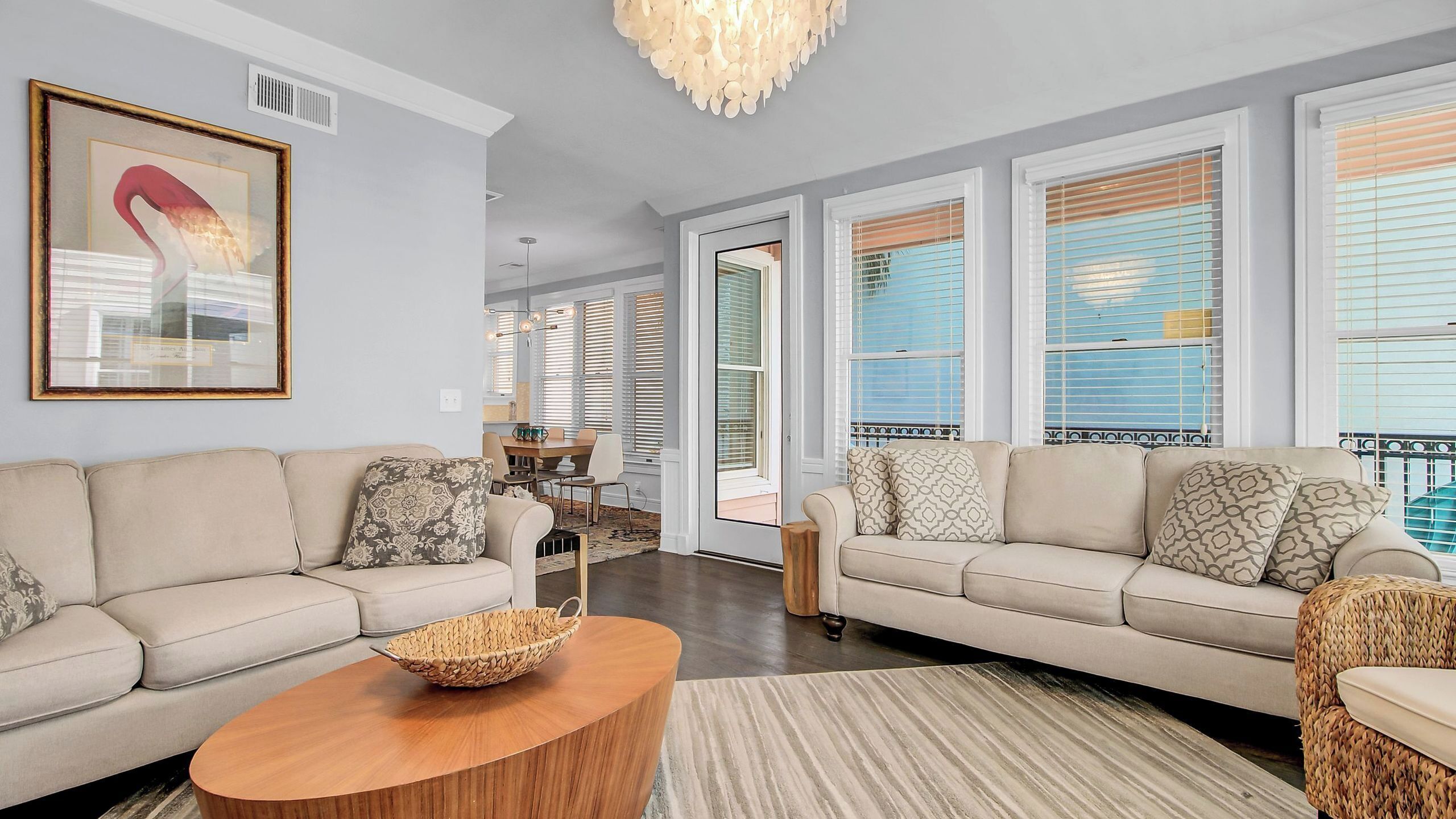 A spacious living room with a large sofa set, a wooden coffee table, and a dining area visible through a glass door.