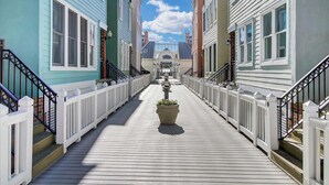 A wooden boardwalk between buildings with white railings and a central planter. - 125 Grand Pavillion by Avantstay Steps From Sand (Isle of Palms)