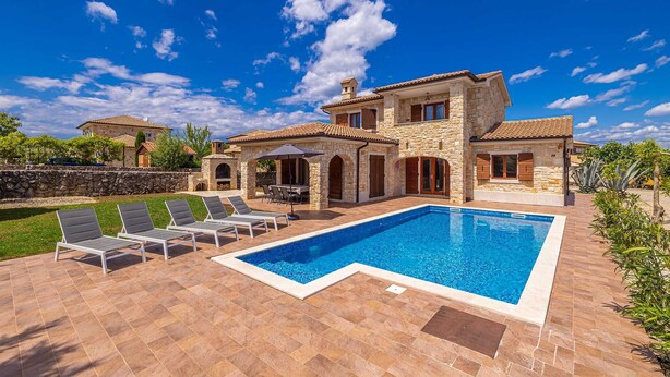 A two-story stone house with a swimming pool, outdoor seating, and a stone wall.