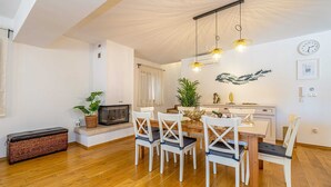 A dining area with a wooden table and white chairs, a fireplace, and a wall-mounted clock.