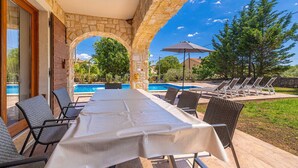 A covered outdoor dining area with a pool in the background.