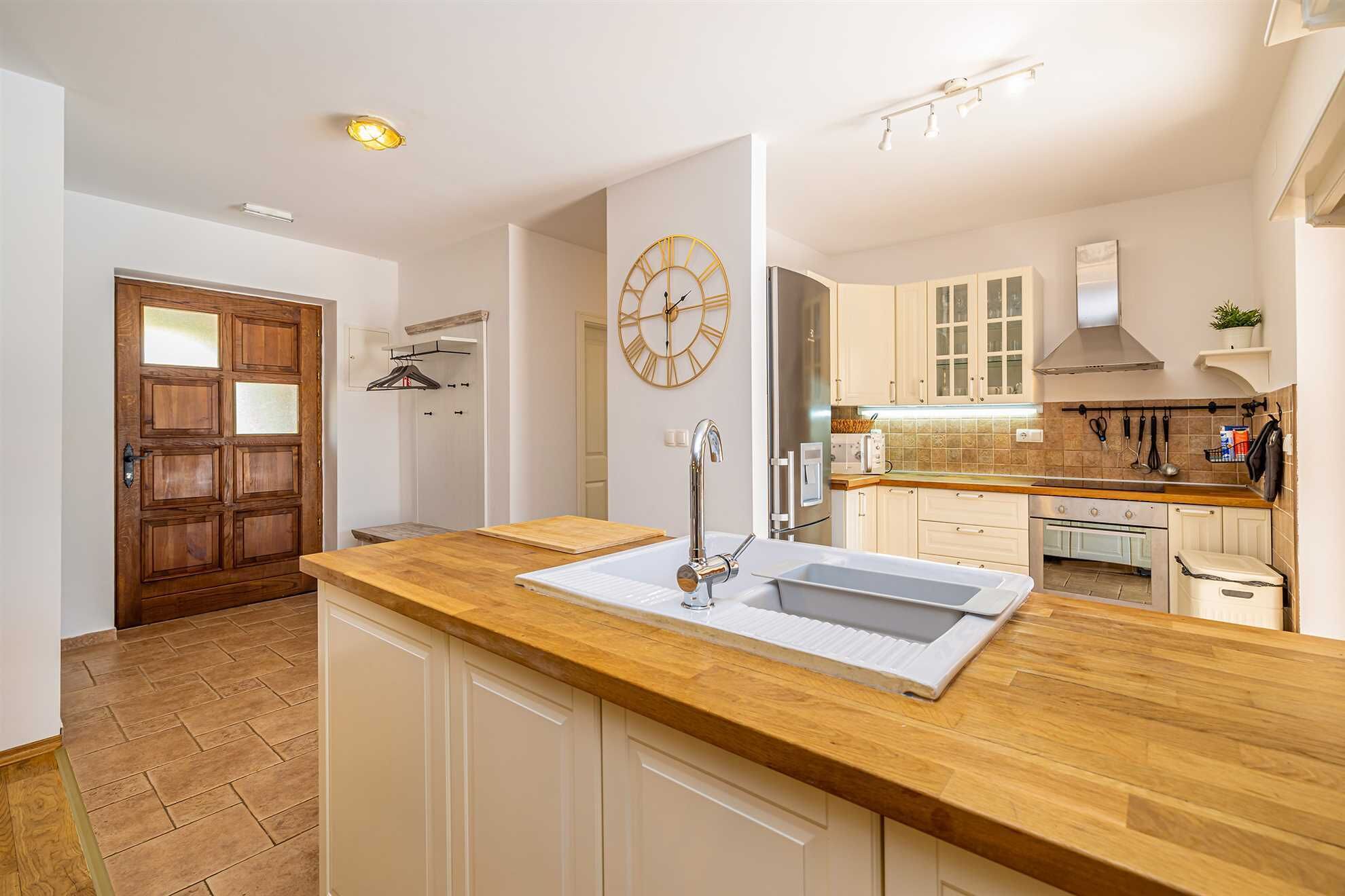 A modern kitchen with a wooden countertop, white cabinets, and a stainless steel sink.