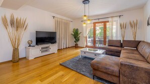 A living room with a flat-screen TV, a brown leather sofa, a white cabinet, and a glass coffee table.