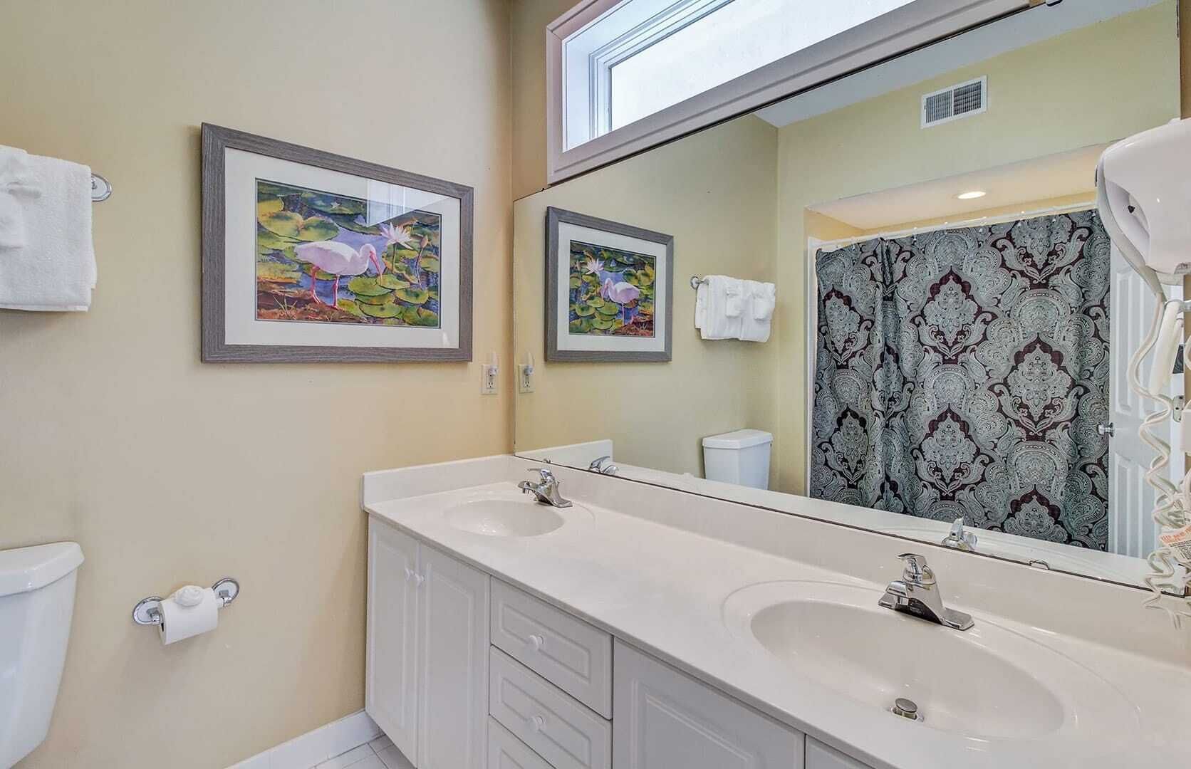 A bathroom with two sinks, a toilet, and a shower curtain with a patterned design.