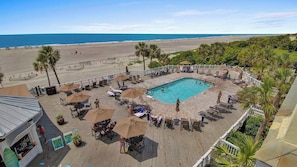 Zona de piscina con sillones de descanso y sombrillas, rodeada por una terraza con vista a la playa y al océano.