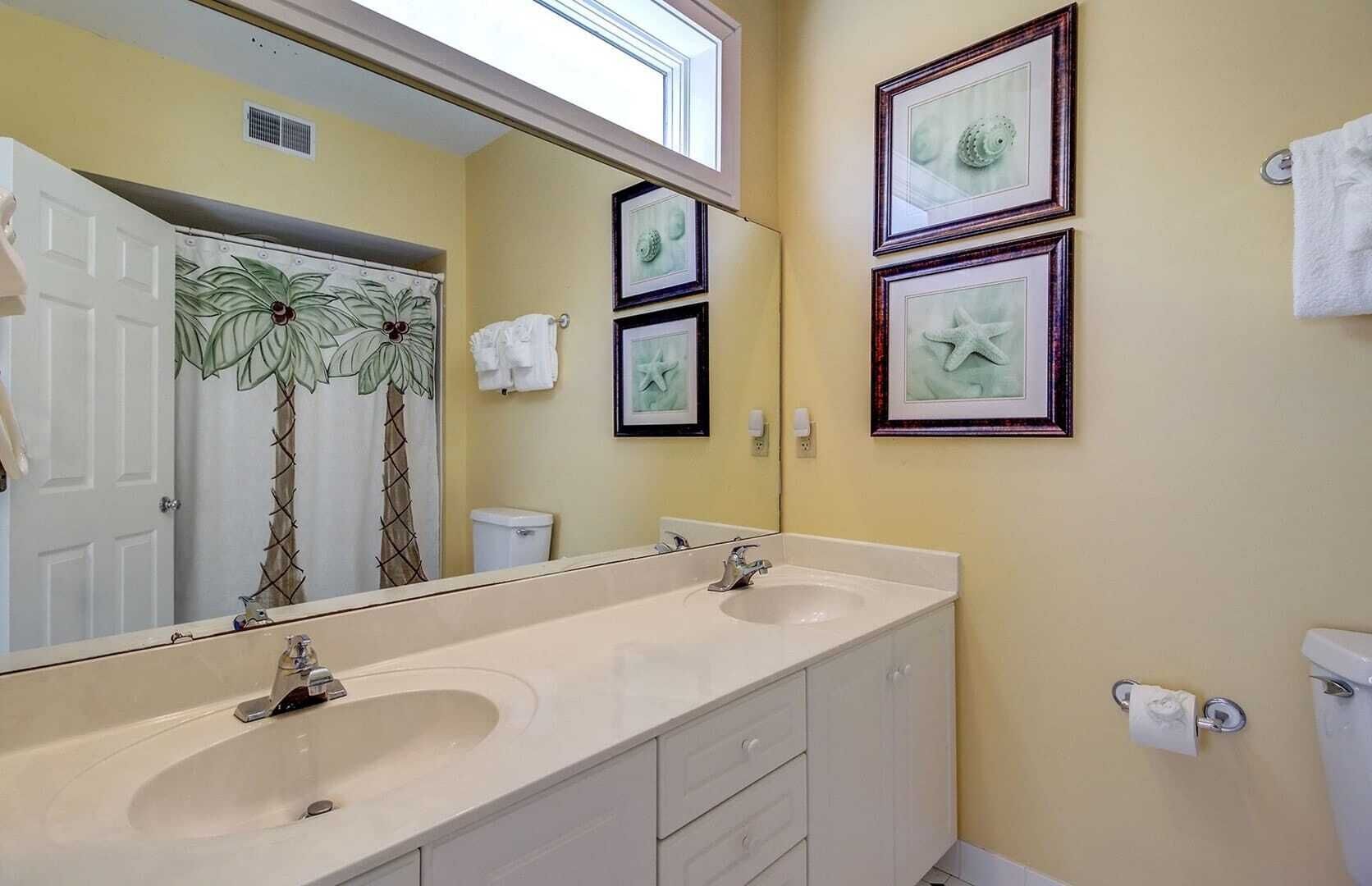 A bathroom with a double sink vanity, a large mirror, and three framed pictures on the wall.