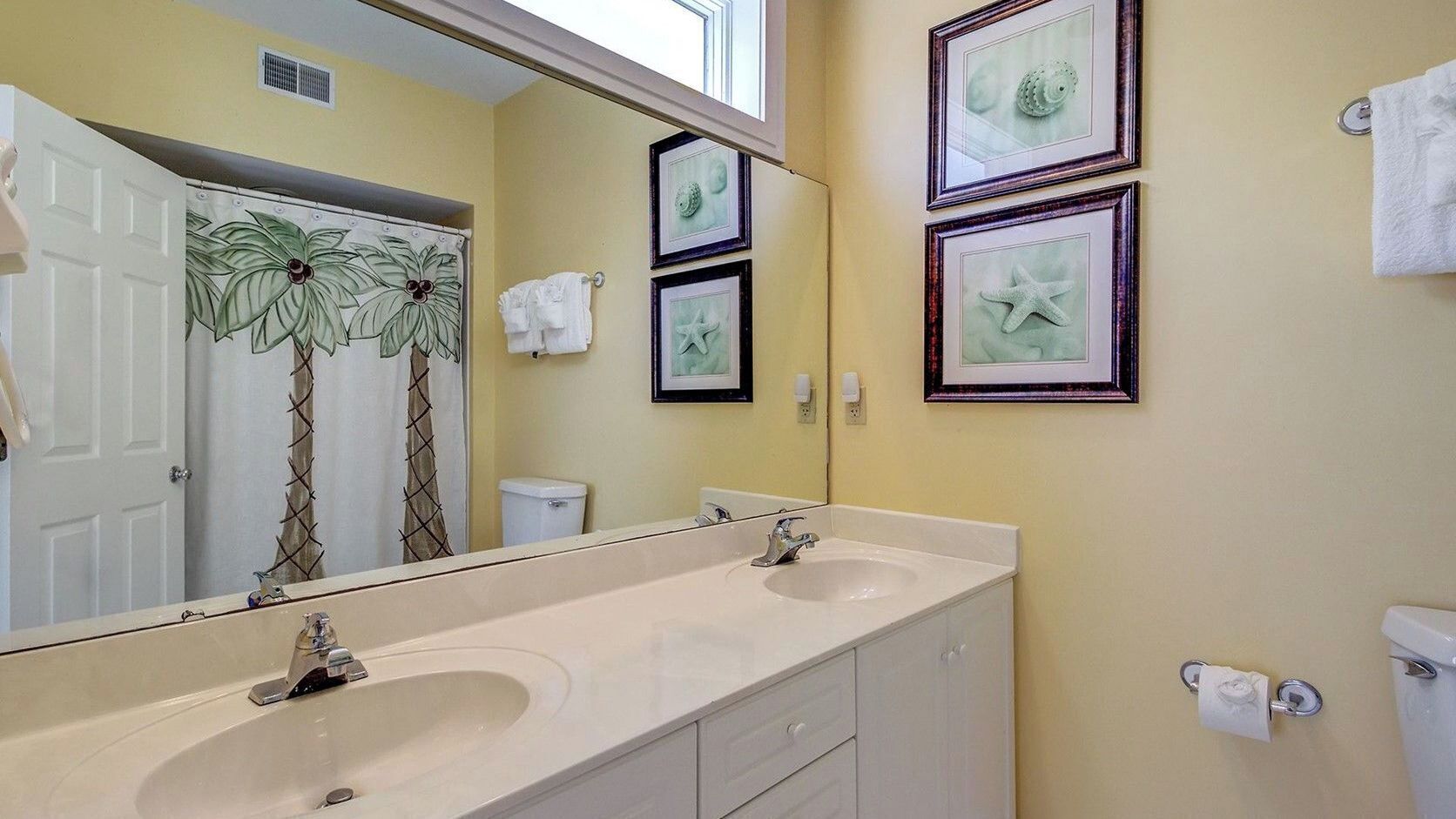 A bathroom with two sinks, a large mirror, and framed pictures on the wall.