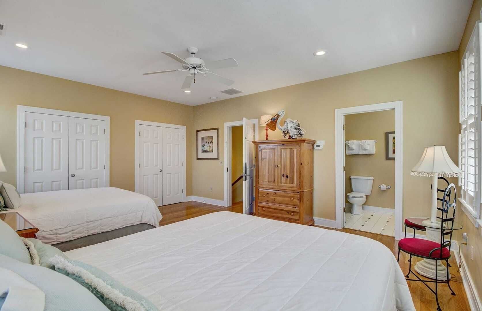 A bedroom with two beds, a wardrobe, a ceiling fan, and a bathroom visible through an open door.