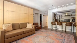 Una sala de estar moderna con un sofá, un tapete estampado y una zona de cocina con taburetes de bar.