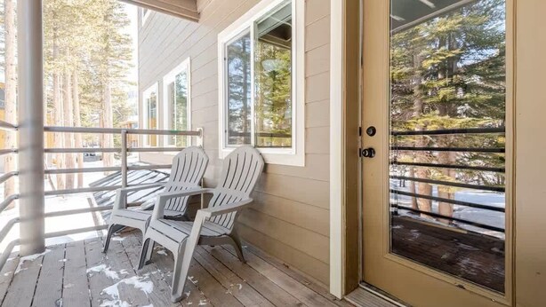 Una terraza de madera con dos sillas Adirondack, un puerta de vidrio y vistas a árboles.