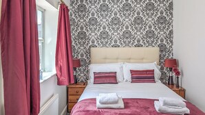 Un letto rifatto con due cuscini, una lampada da comodino e una finestra con tende rosse.