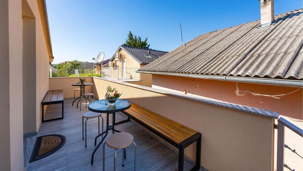 A balcony with a wooden bench, two chairs, and a small round table with a vase of flowers. - Beautiful apartment in Gornji Karin with WiFi (Gornji Karin)