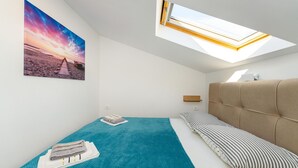 A bedroom with a bed, a skylight, a beach sunset painting, and a small bedside table. - Beautiful apartment in Gornji Karin with WiFi (Gornji Karin)