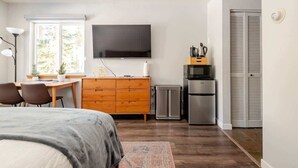 Ein Schlafzimmer mit Bett, Schreibtisch, Fernseher, Küchenzeile und Kleiderschrank.